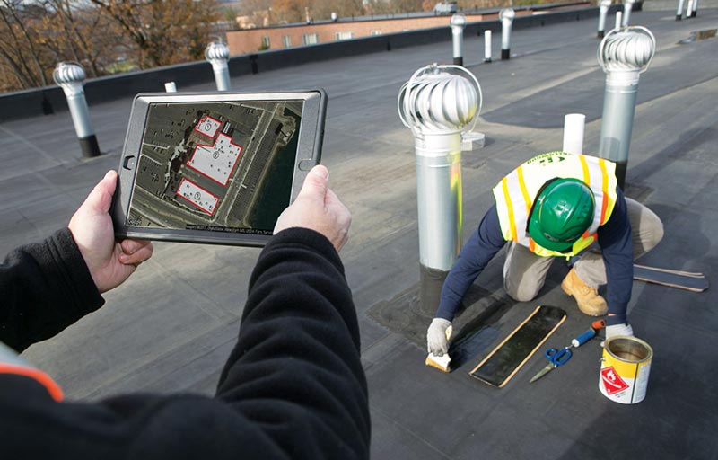 Greenwood Roof Services - workers at a job on top of a roof with one holding tablet