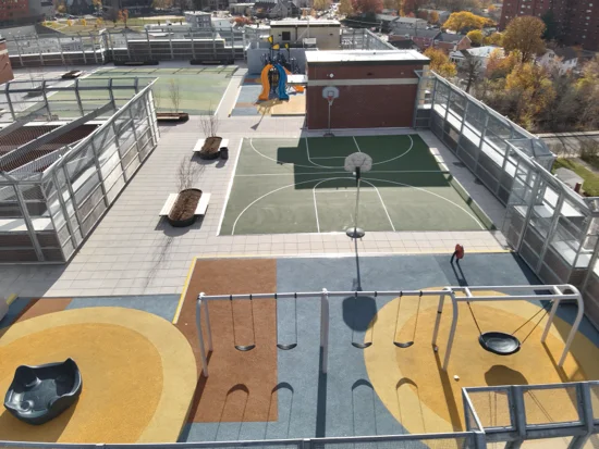 Drone photo of a rooftop playground with a swingset in the foreground and basketball court in the background and surrounding paver deck